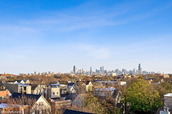 Panoramic view of a city skyline with residential rooftops and trees in the foreground.