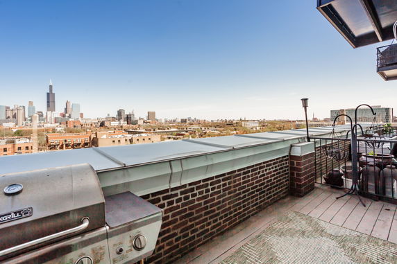 Rooftop view with city skyline in the background and a barbecue grill in the foreground.
