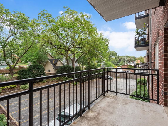 View from a balcony overlooking a parking area and surrounding houses with trees nearby.