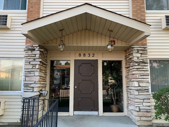Front view of a multi-story building entrance with stone and siding facade.