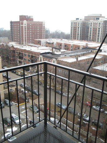 Aerial view of an urban area with multiple buildings and a metal balcony railing in the foreground.