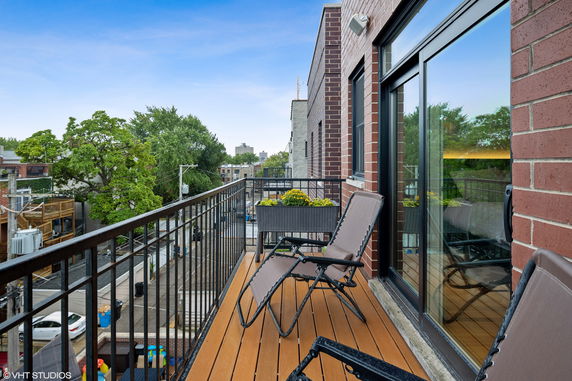 View from a balcony with chairs, overlooking a street and surrounding trees and buildings.