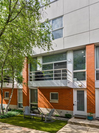 Front view of a contemporary multi-story building with large windows and a small outdoor seating area.