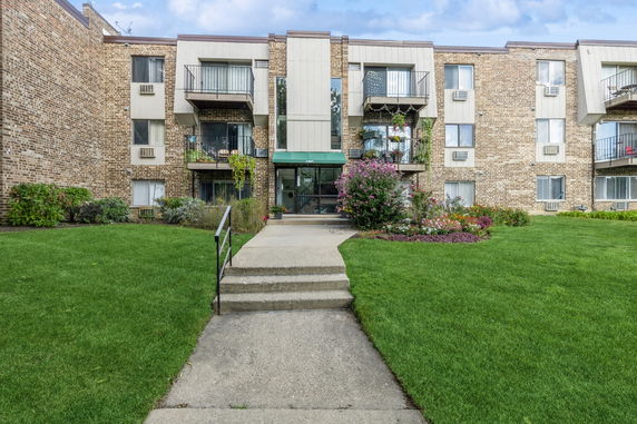 Front view of a multi-story brick building with balconies and landscaped entrance.