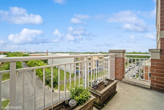 Panoramic view from a building balcony with railing and planters, overlooking a street and surrounding buildings.