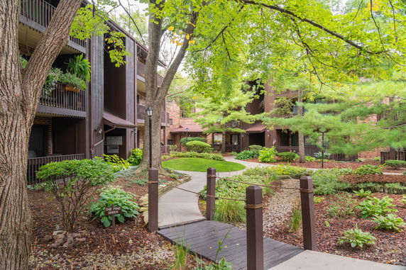 Front view of a multi-story building with balconies surrounded by trees and landscaped garden.