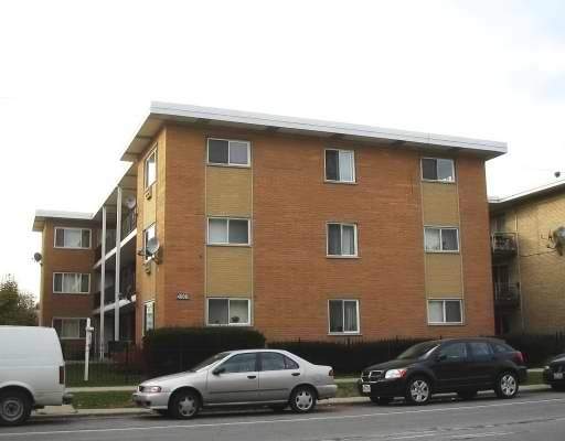 Front view of a multi-story brick apartment building with parked cars in front.