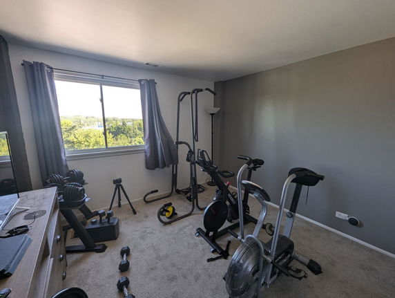 Indoor room with exercise equipment including a stationary bike and weights.