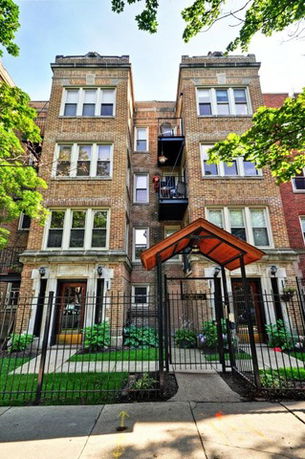Front view of a multi-story brick apartment building with a gated entrance.