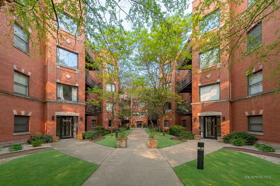 Front view of brick apartment buildings with an entrance pathway and landscaped area.