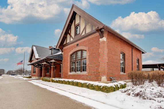 Front view of a brick building with a gabled roof and large windows.