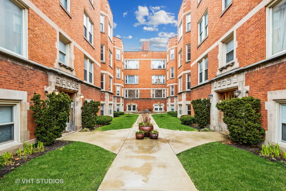 Front view of a red-brick apartment complex featuring multiple stories and symmetrical architecture.