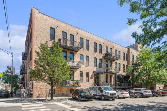 Front view of a multi-story brick building with balconies and parked cars.