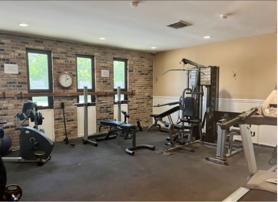 Room containing various exercise equipment including a treadmill, weight machines, and stationary bikes.