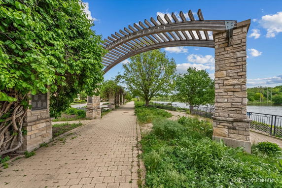 Stone and wood archway at the entrance of a park walkway surrounded by greenery.
