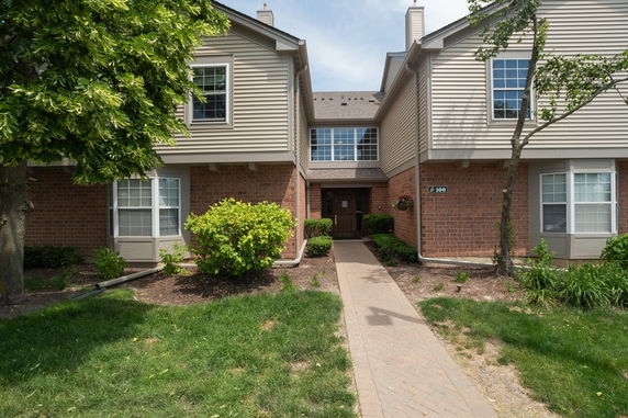 Front view of a two-story residential building with a brown brick and beige siding exterior.