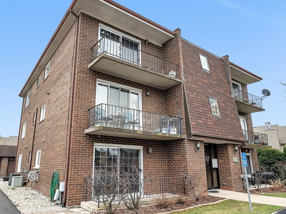 Front view of a three-story brick apartment building with balconies.