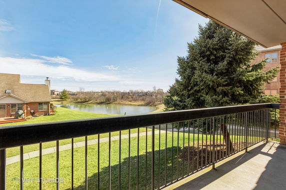 Panoramic view from a building showing a scenic landscape with a pond, trees, and surrounding houses.