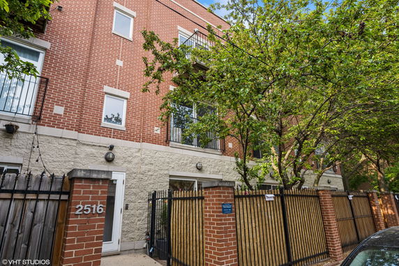 Front view of a multi-story brick building with balconies and a gated entrance.