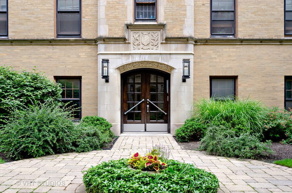 Front view of a building entrance with decorative stone arch and wooden doors.