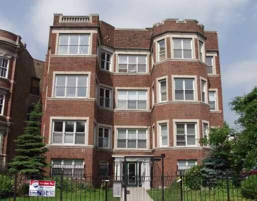 Front view of a multi-story brick apartment building with large windows and a gated entrance.