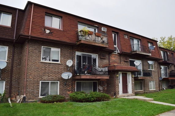 Front view of a three-story brick apartment building with multiple balconies and satellite dishes.