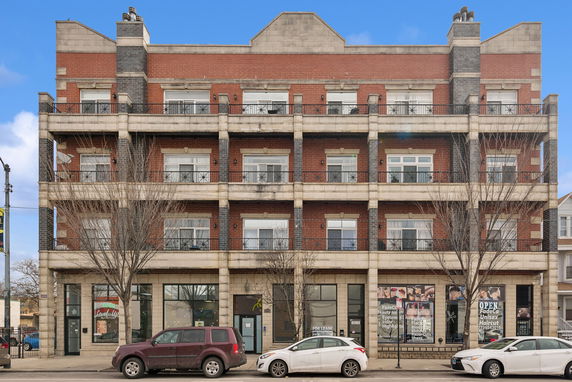 Front view of a multi-story brick building with multiple balconies and ground-floor commercial spaces.