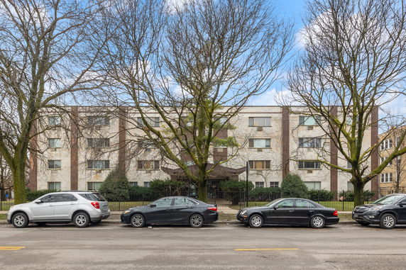 Front view of a multi-story apartment building with several cars parked on the street.