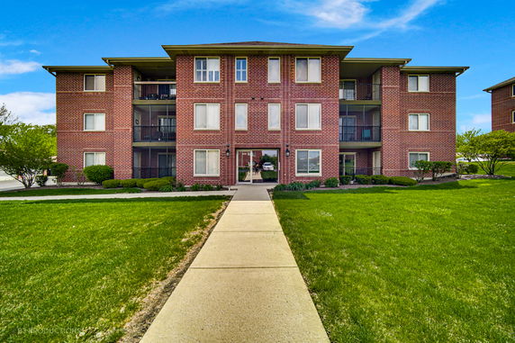 Front view of a three-story brick apartment building with balconies.