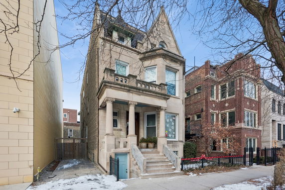 Front view of a multi-story stone house with a classic architectural design and columns.