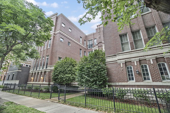 Front view of a large brick building with multiple windows and a gated entrance.