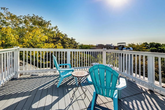 Rooftop patio with chairs and table, surrounded by white railing and trees in the background.