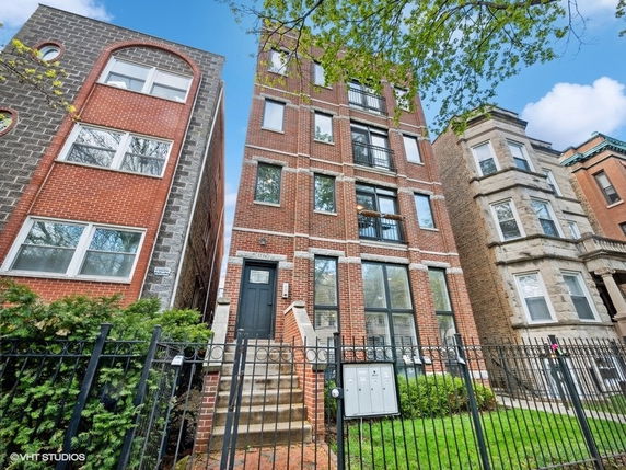 Front view of a multi-story brick building with a black door and metal railings on the entrance stairs.