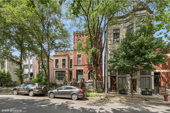 Front view of a brick residential building with large windows and a tree-lined street.