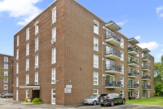 Front view of a multi-story brick apartment building with balconies and a parking area.