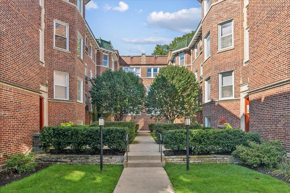 View of a brick apartment building with multiple windows and landscaped entrance.