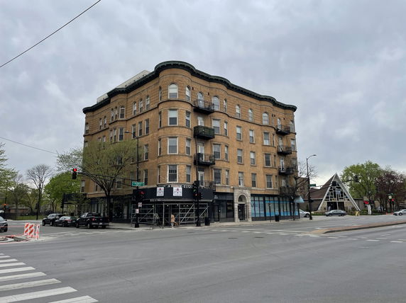 Front view of a multi-story brick building with balconies on a street corner.