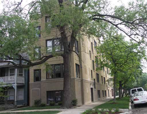 Front view of a multi-story residential building with large windows and surrounded by trees.