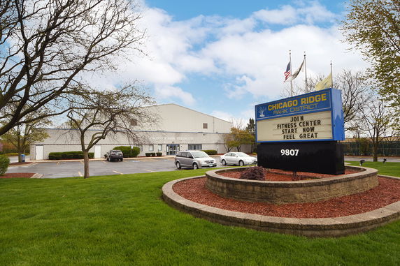 Front view of a large fieldhouse building with a parking area in front.