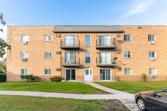 Front view of a three-story brick apartment building with balconies.