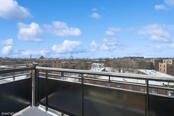 Panoramic view from a balcony overlooking buildings and a snowy landscape under a blue sky with clouds.