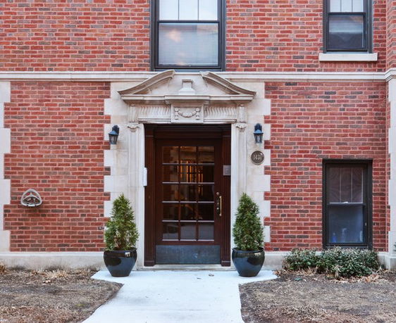 Front view of a brick building entrance with decorative stonework and two planters.