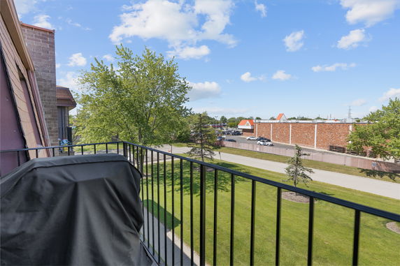 Balcony view overlooking a grassy area and a parking lot with buildings in the distance.