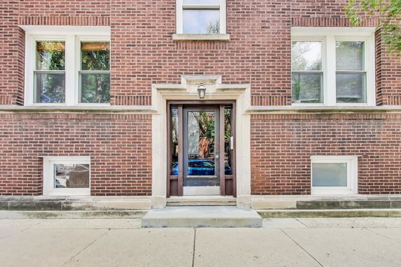 Front view of a brick apartment building entrance with multiple windows and a glass door.