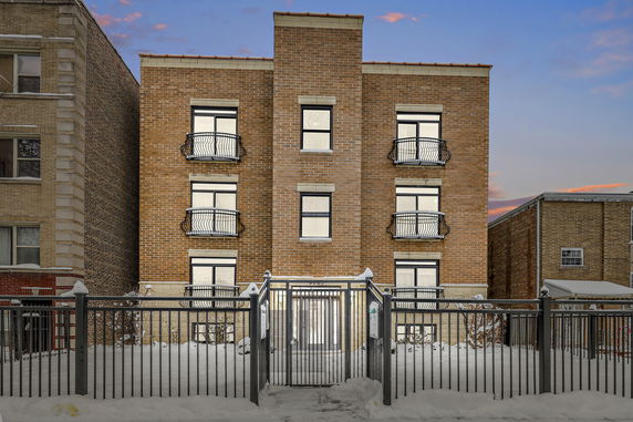 Front view of a three-story brick building with a metal fence and balconies on each floor.