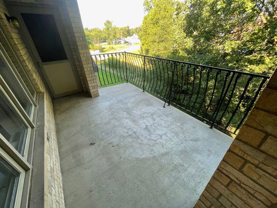 Concrete balcony with metal railing and view of surrounding greenery.