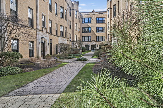 Front view of a multi-story apartment building with a pathway and gardens.