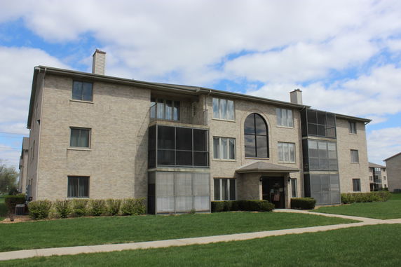 Front view of a multi-story apartment building with large windows and enclosed balconies.