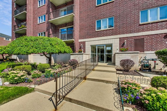 Front view of a multi-story brick building with balconies and a landscaped entrance.