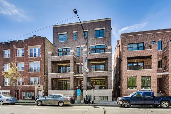 Front view of a multi-story apartment building with balconies and large windows.